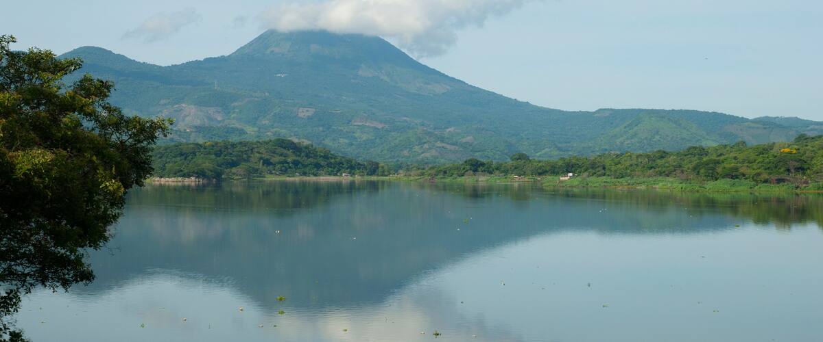A calm lake with a mountain in the background and some trees in the foreground.