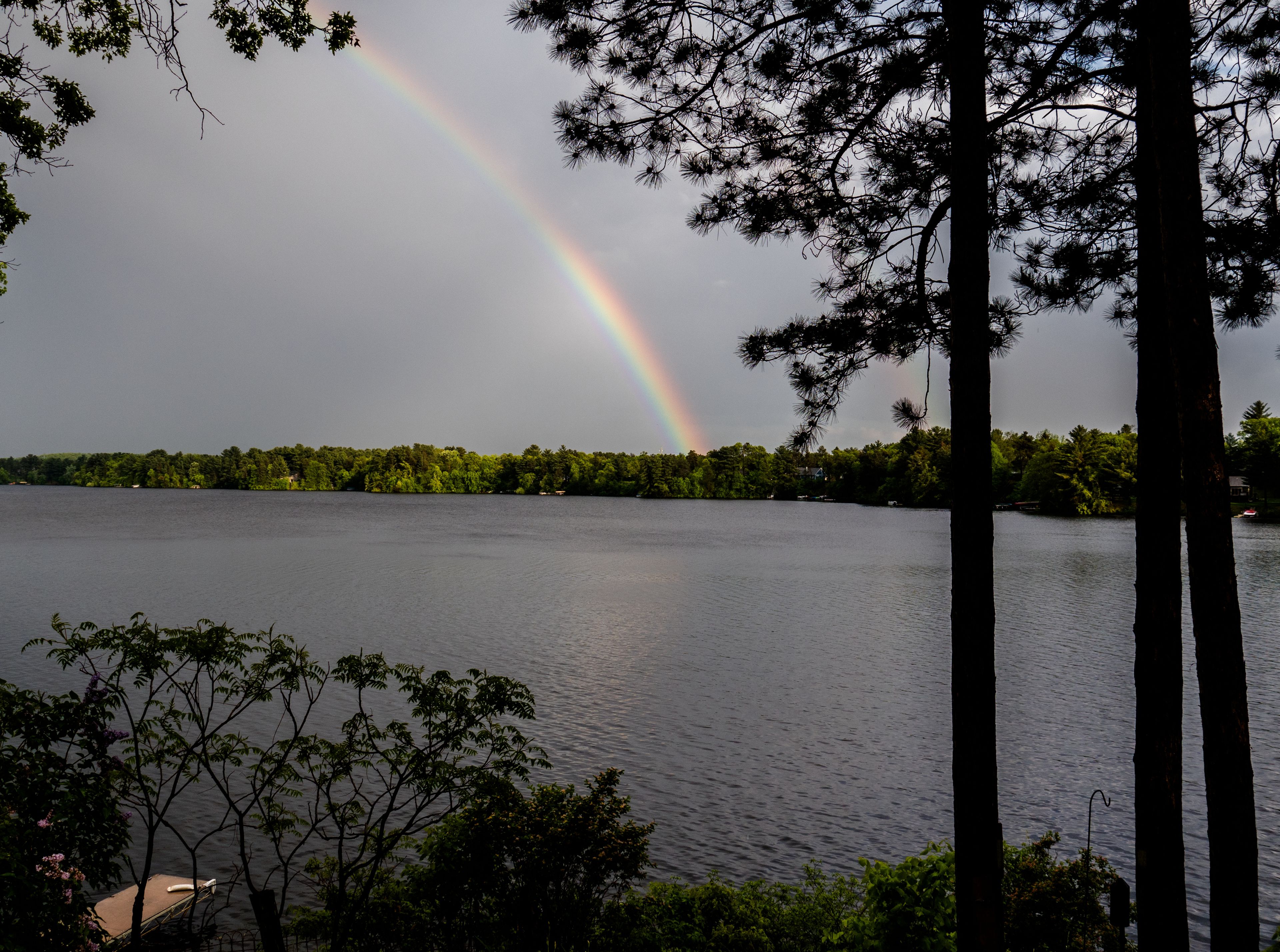 Un lac où se reflète un arc-en-ciel, entouré d’arbres et surplombé d’un ciel nuageux.