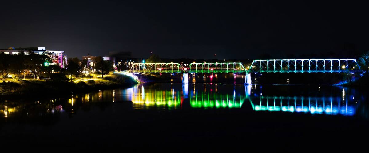 A brightly lit bridge at night with reflections on the water.
