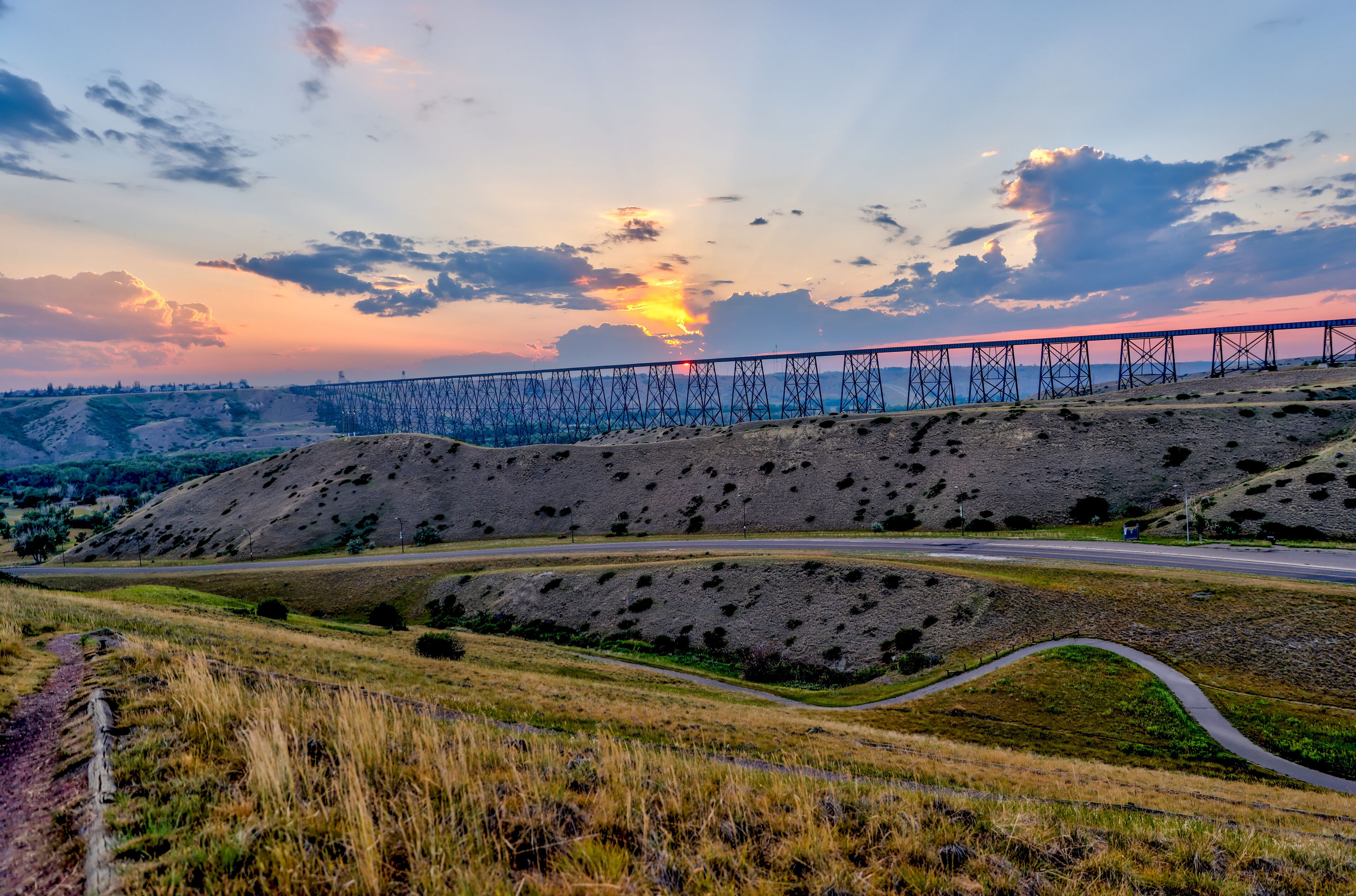 A sunset over a bridge, a winding road, and a hilly landscape.
