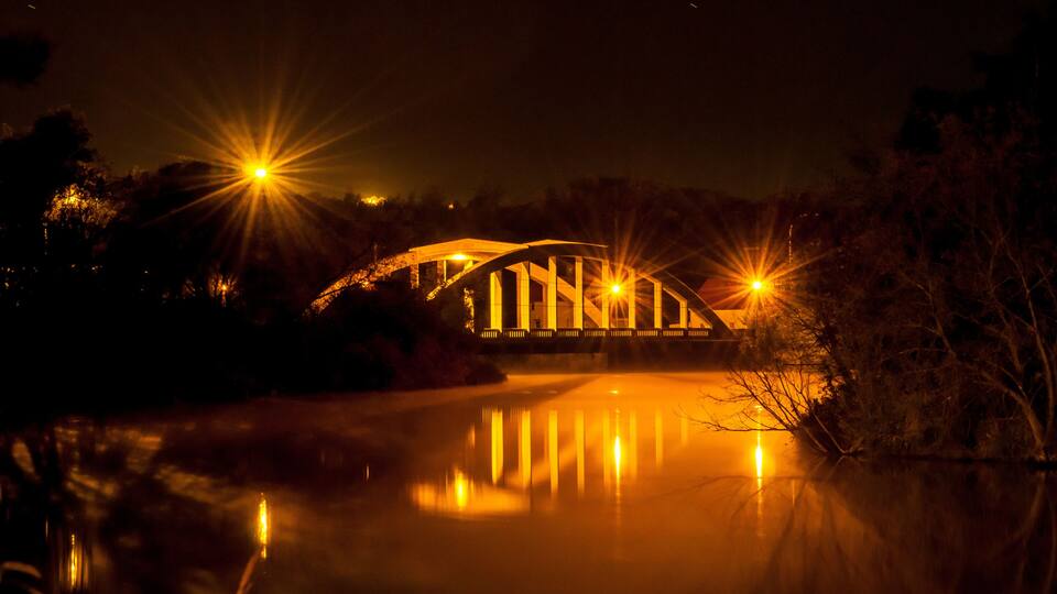 A bridge at night with lights reflecting on the water.