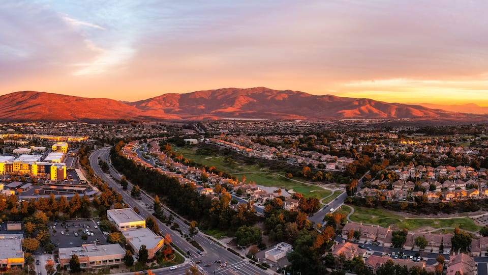 A cityscape with a river, mountains, and autumn foliage.
