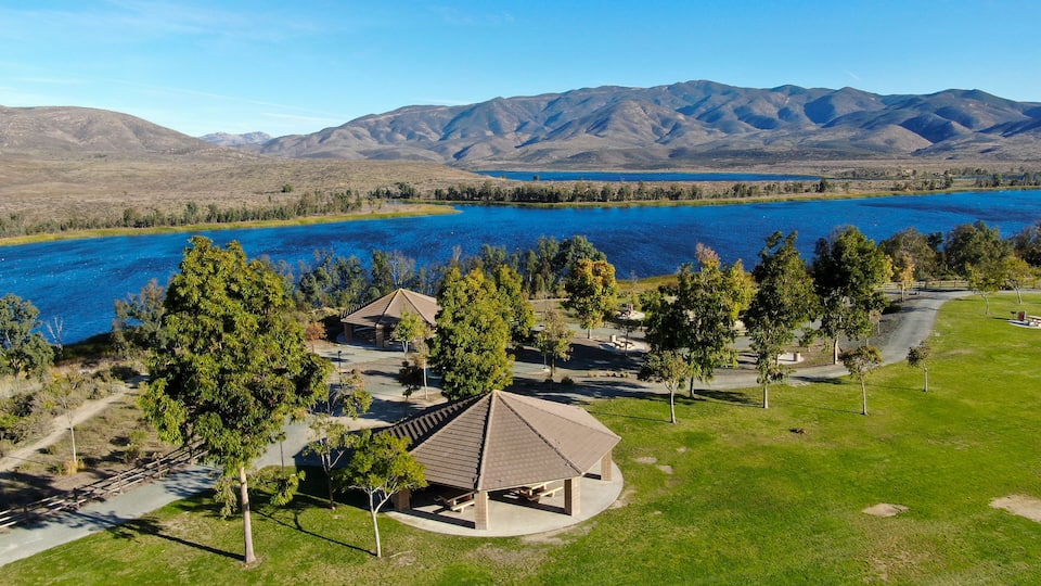 A lakeside view with a gazebo, trees, and mountains in the background.