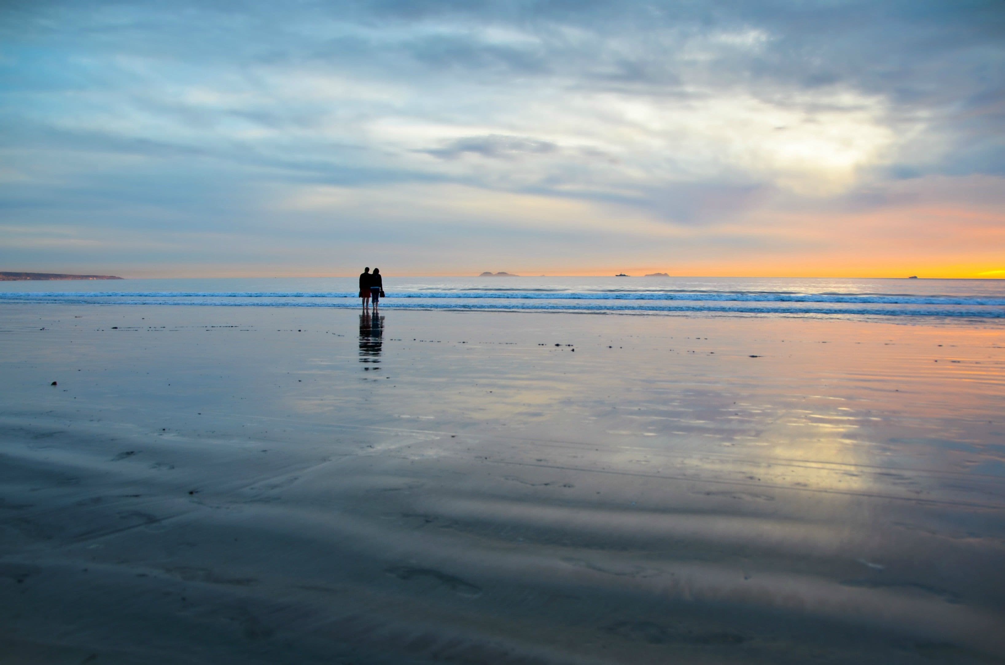 Una playa con dos personas caminando hacia el océano al atardecer.