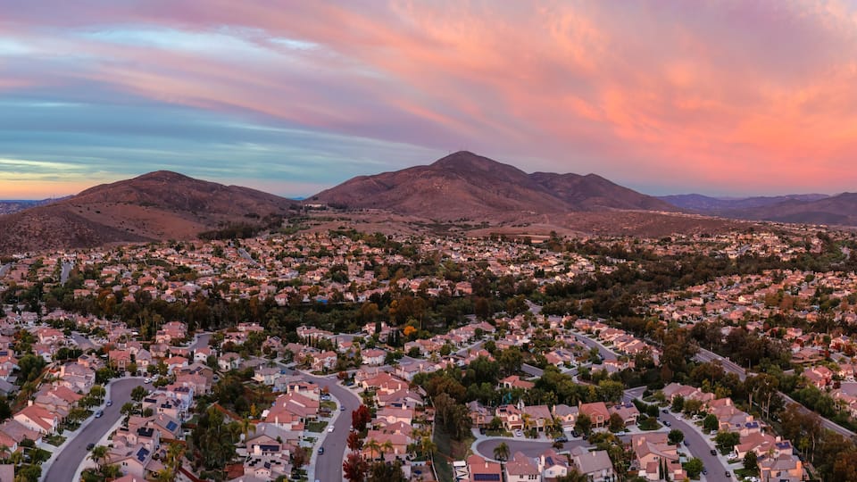A residential area with houses, roads, and mountains in the background.