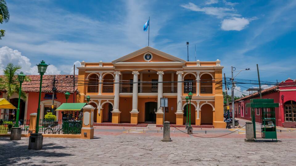 A colonial-style building with a central dome and columns, surrounded by cobblestone streets and palm trees.