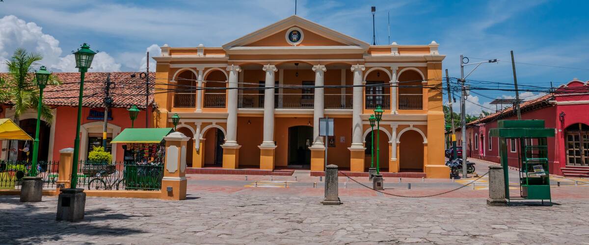 A colonial-style building with a central dome and columns, surrounded by cobblestone streets and palm trees.