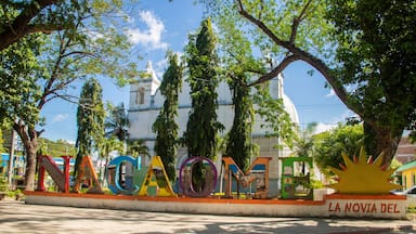 A colorful sign with the letters "NACAO" and "LA NOVIA DEL" in a public square with trees and a white building in the background.