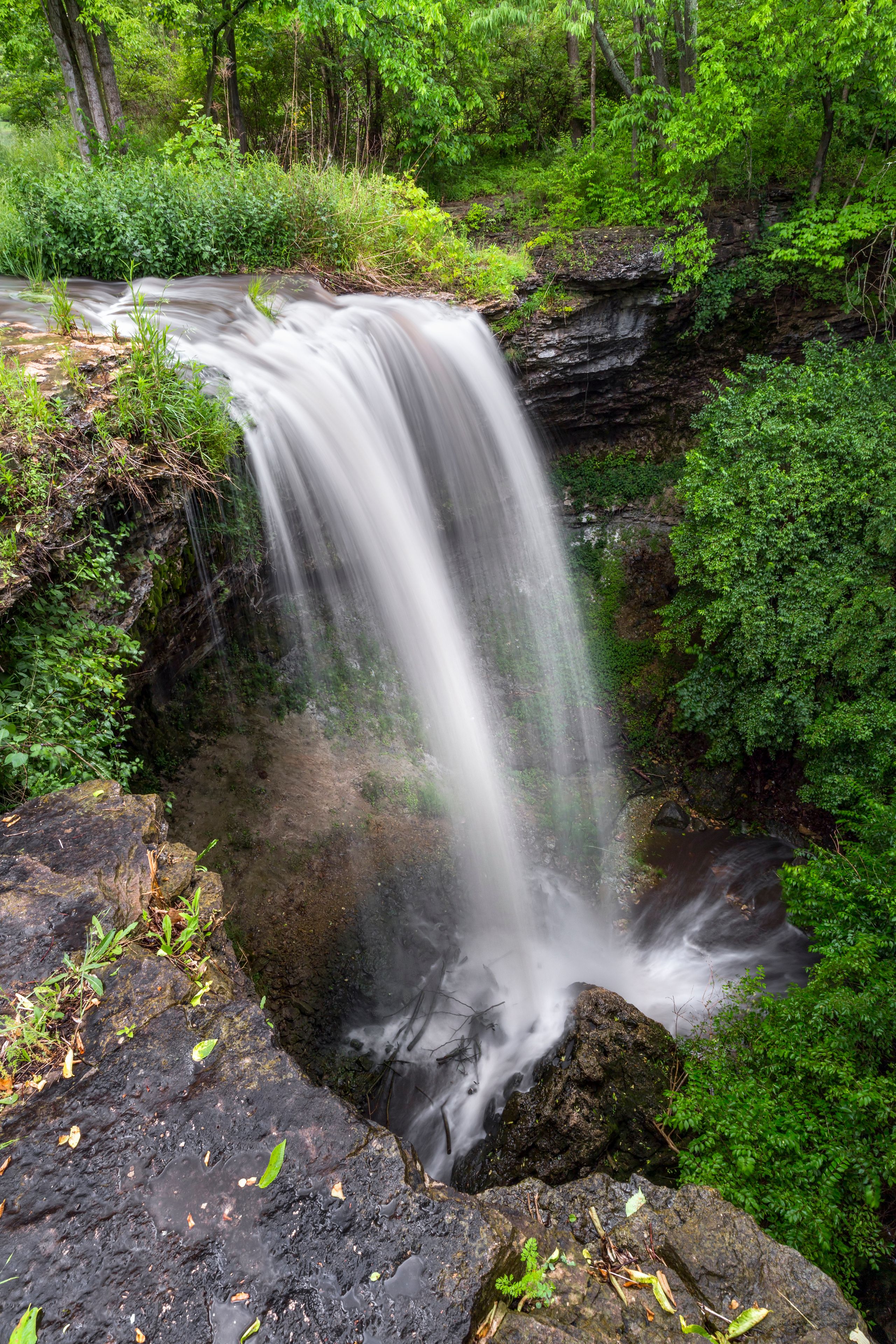 A waterfall cascading over a rocky ledge surrounded by lush greenery.