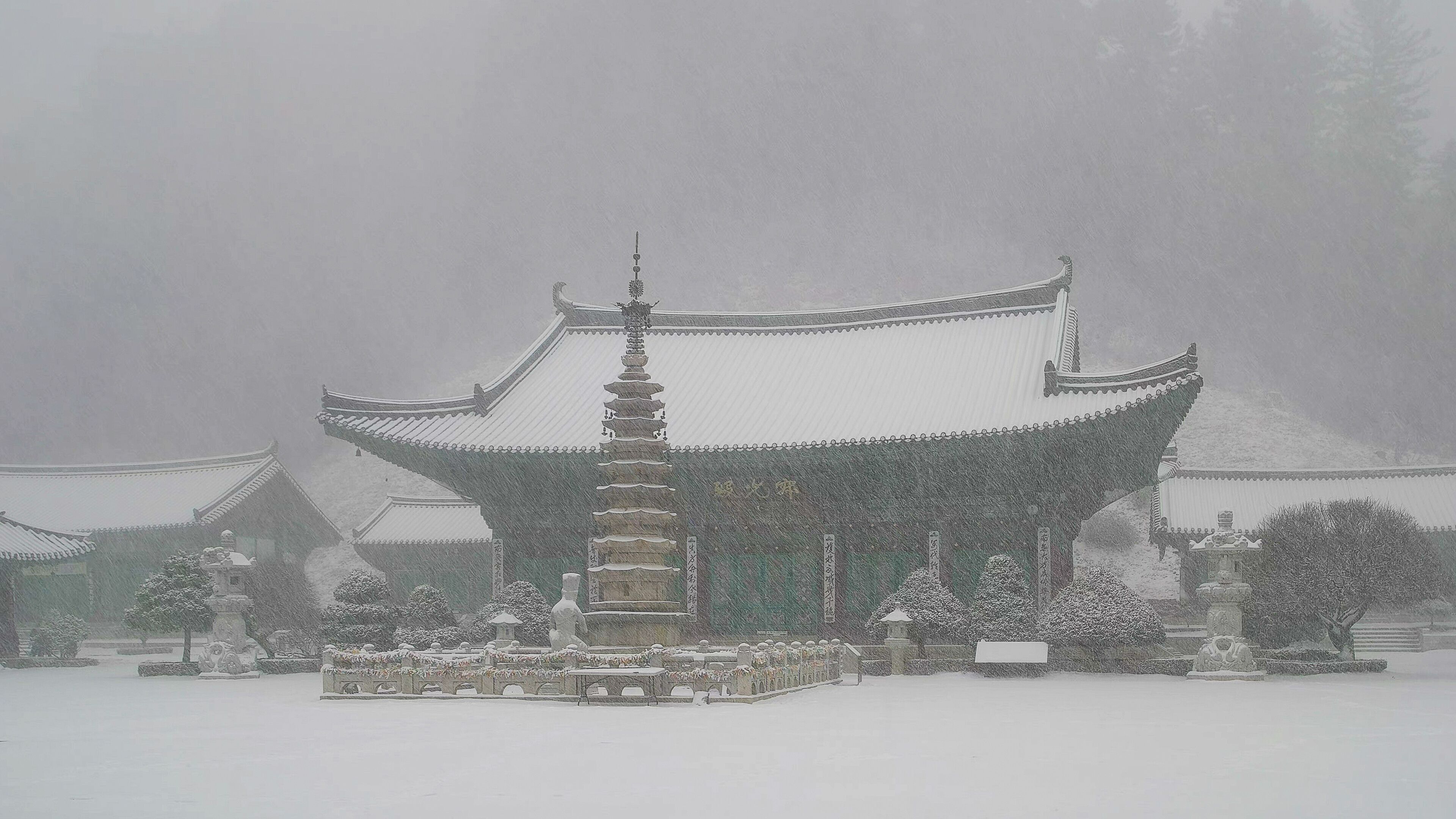 A traditional East Asian temple with a multi-tiered pagoda, surrounded by snow-covered trees and a serene landscape.