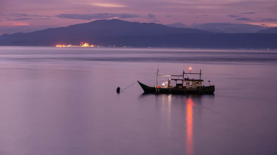 A boat anchored in calm waters with a mountain range in the background.