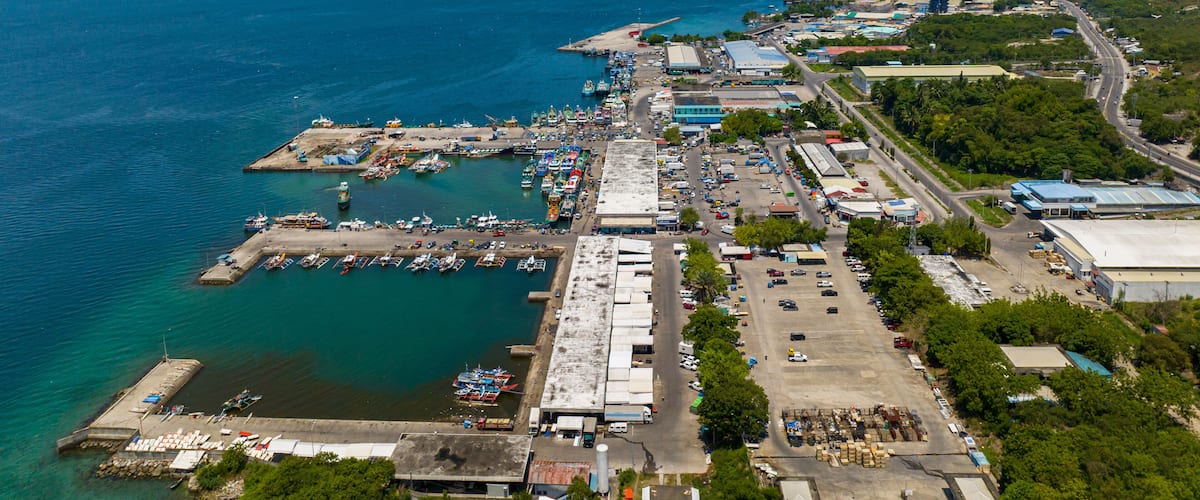 An aerial view of a coastal town with a marina, industrial buildings, and a clear blue sky.