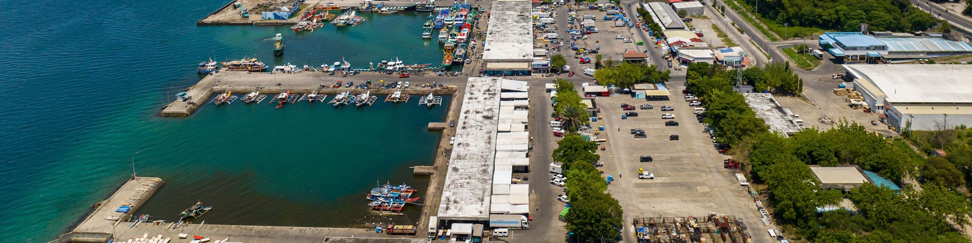 An aerial view of a coastal town with a marina, industrial buildings, and a clear blue sky.
