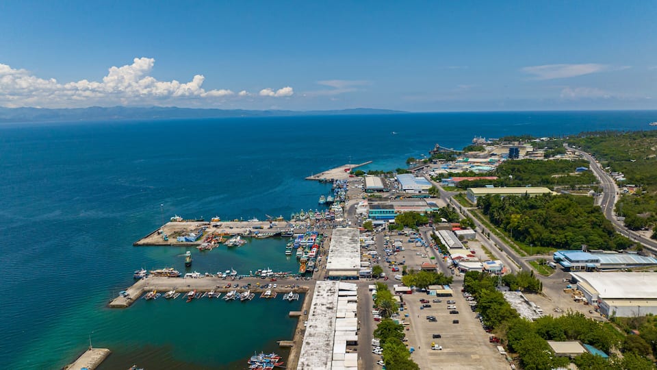 An aerial view of a coastal town with a marina, industrial buildings, and a clear blue sky.