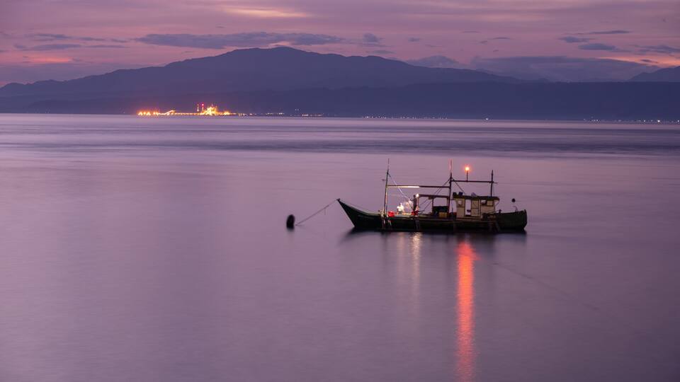 A boat anchored in calm waters with a city skyline in the distance.