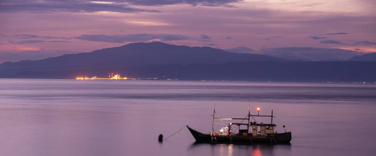 A boat anchored in calm waters with a city skyline in the distance.