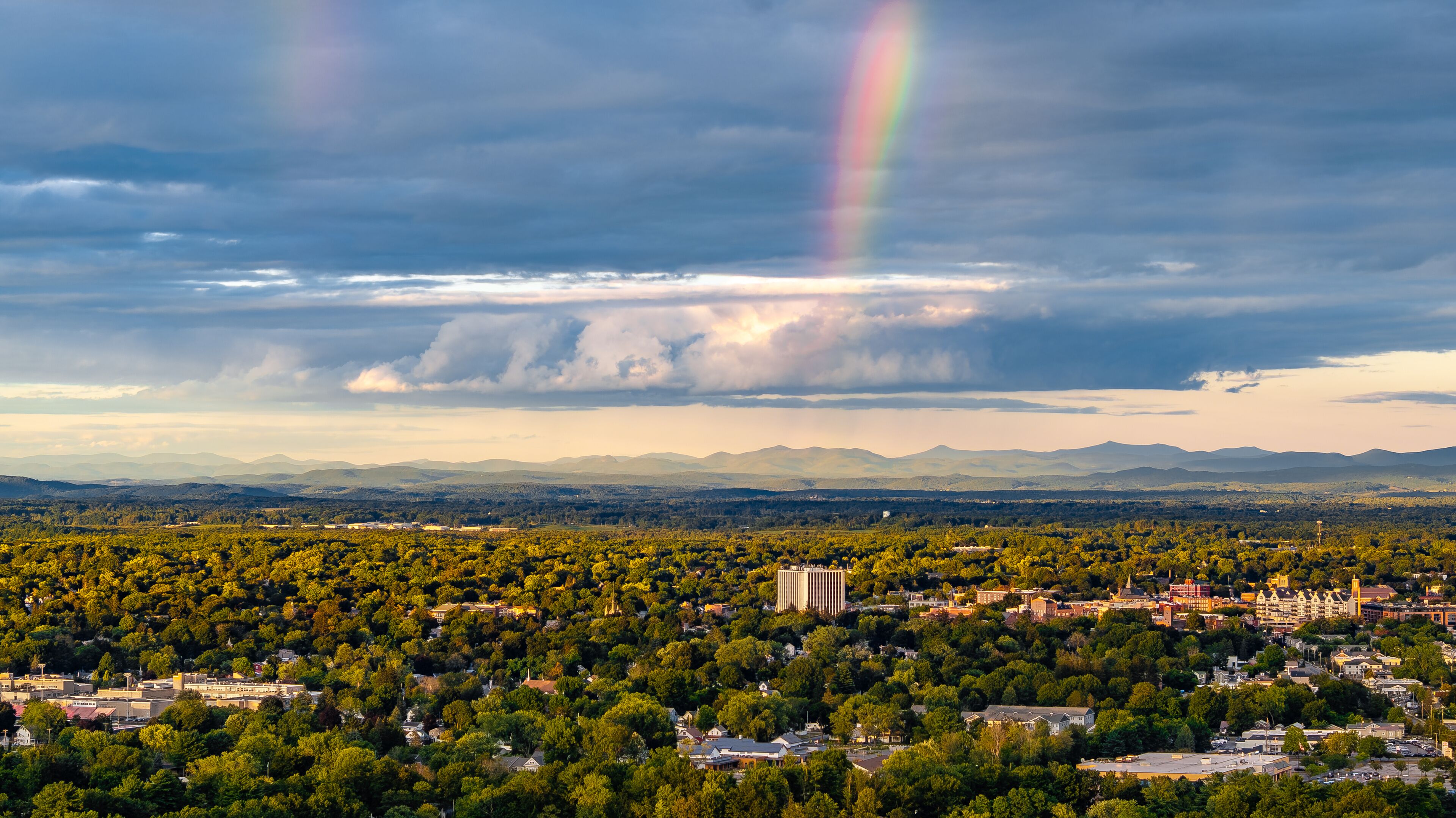 A cityscape with a rainbow, mountains, and a cloudy sky.