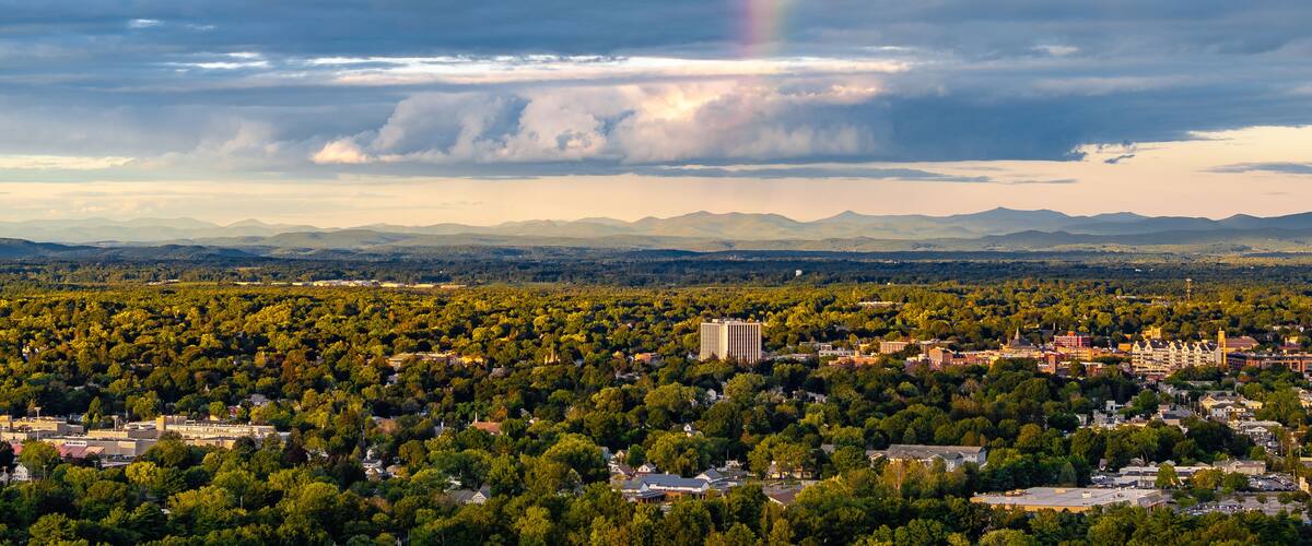 A cityscape with a rainbow, mountains, and a cloudy sky.