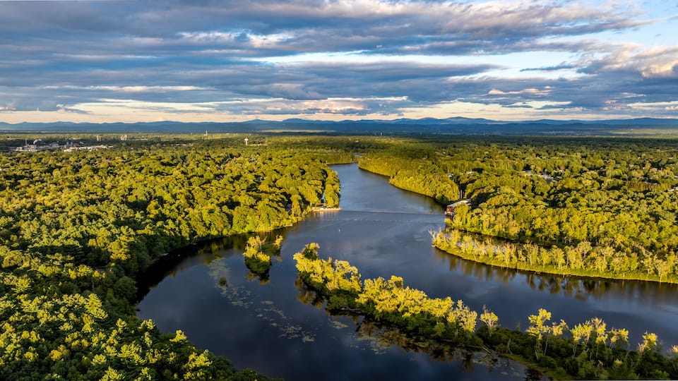 A river winding through a dense forest with a mountainous backdrop.