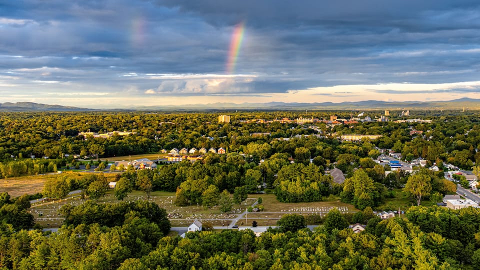 A town with a cemetery, surrounded by dense forests and a rainbow in the sky.