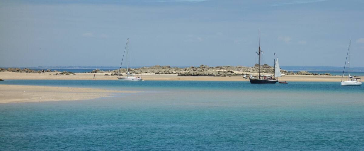 A calm beach with clear turquoise waters, a sandy shore, and several sailboats anchored near the shore.