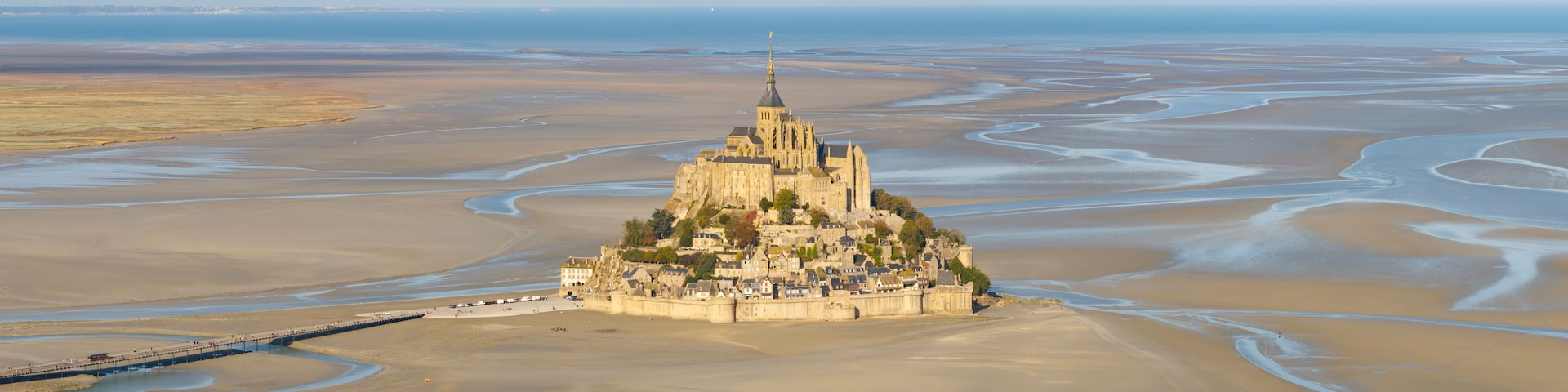 A coastal town with a prominent castle on a hill, surrounded by expansive sandy beaches and tidal flats.