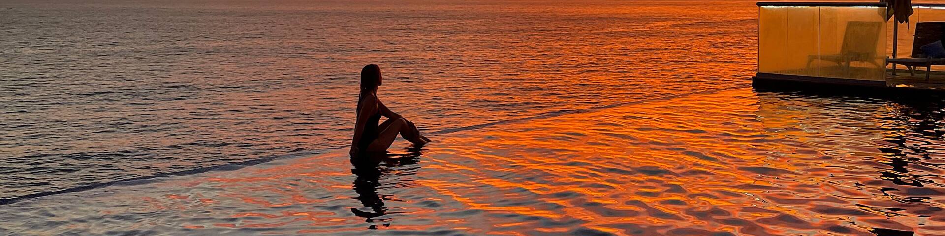 Woman silhouette relaxing in infinity pool at sunset over Pacific Ocean in La Libertad, El Salvador. Tropical travel destination and wide copy space for text.