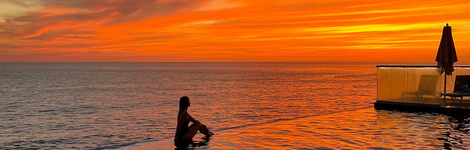 Woman silhouette relaxing in infinity pool at sunset over Pacific Ocean in La Libertad, El Salvador. Tropical travel destination and wide copy space for text.