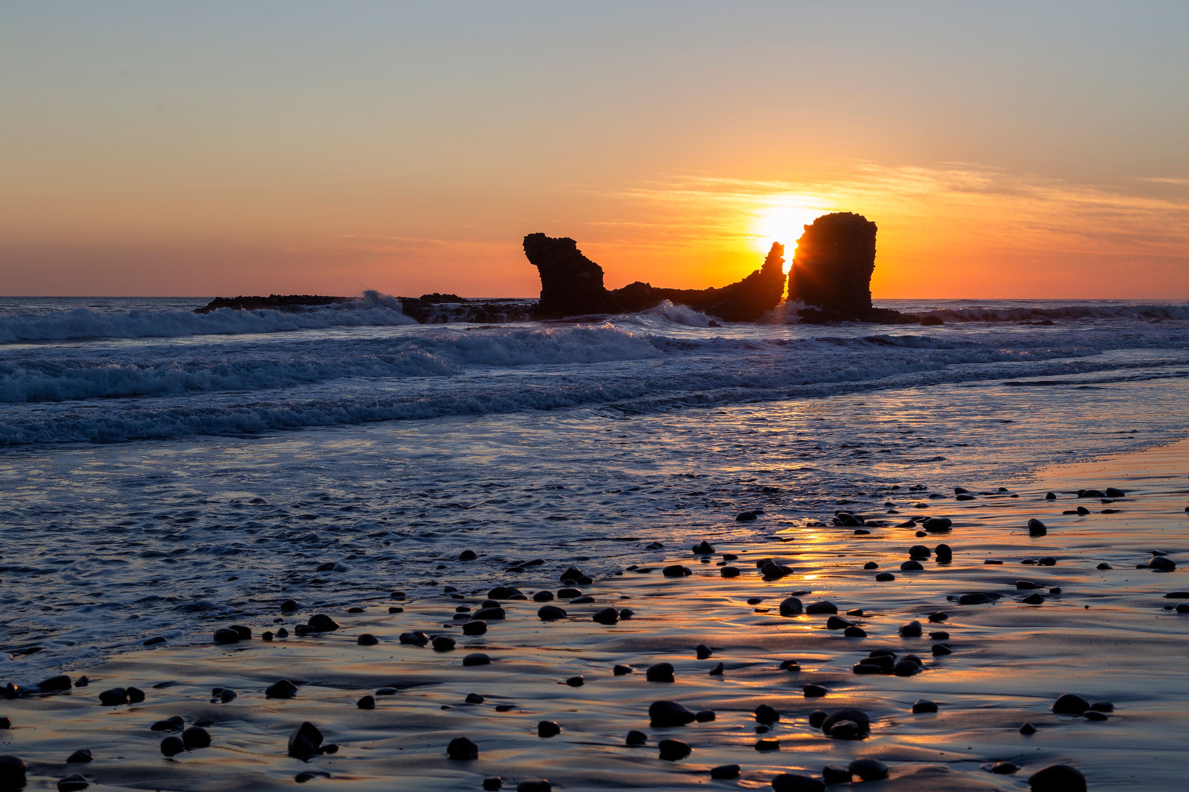 Playa El Tunco, a popular surf beach in El Salvador. Sunset with the iconic rock stack and reflections on the sand. Quiet, peaceful beach scene.
