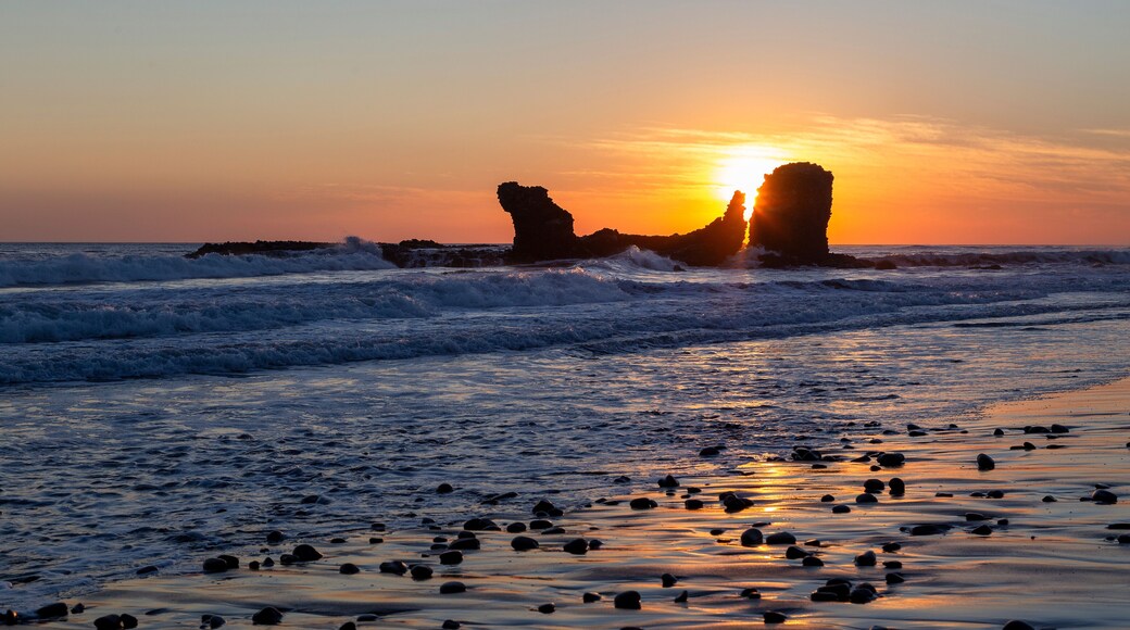 Playa El Tunco, a popular surf beach in El Salvador. Sunset with the iconic rock stack and reflections on the sand. Quiet, peaceful beach scene.