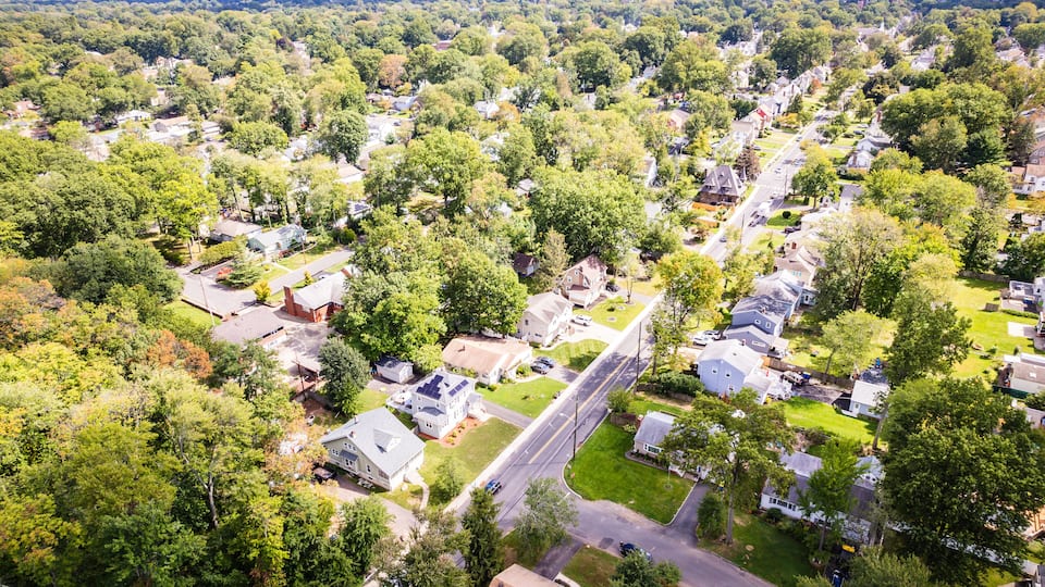 An aerial view of a suburban neighborhood with houses, roads, and surrounding greenery.