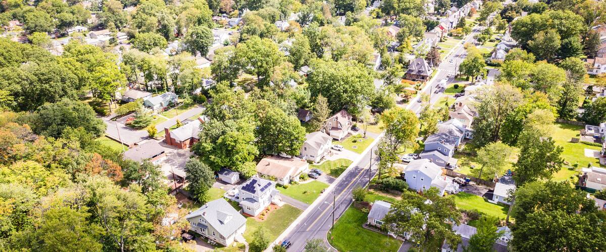 An aerial view of a suburban neighborhood with houses, roads, and surrounding greenery.