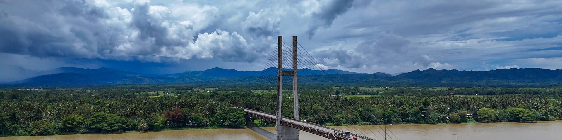 Uma ponte suspensa sobre um rio, com montanhas ao fundo.