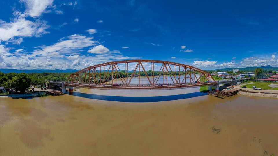 A large metal bridge over a river with a town in the background.