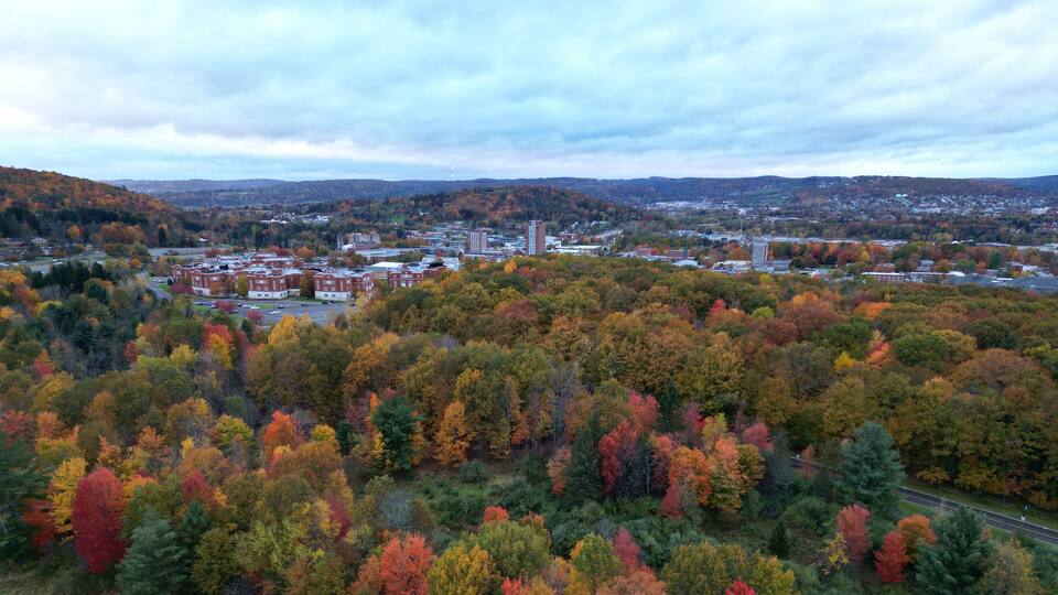 arial view of binghamton university in vestal, new york during autumn with fall foliage (leaves changing colors) at dusk, sunset, cloudy sky (library tower, student union, mountainview residence hall)