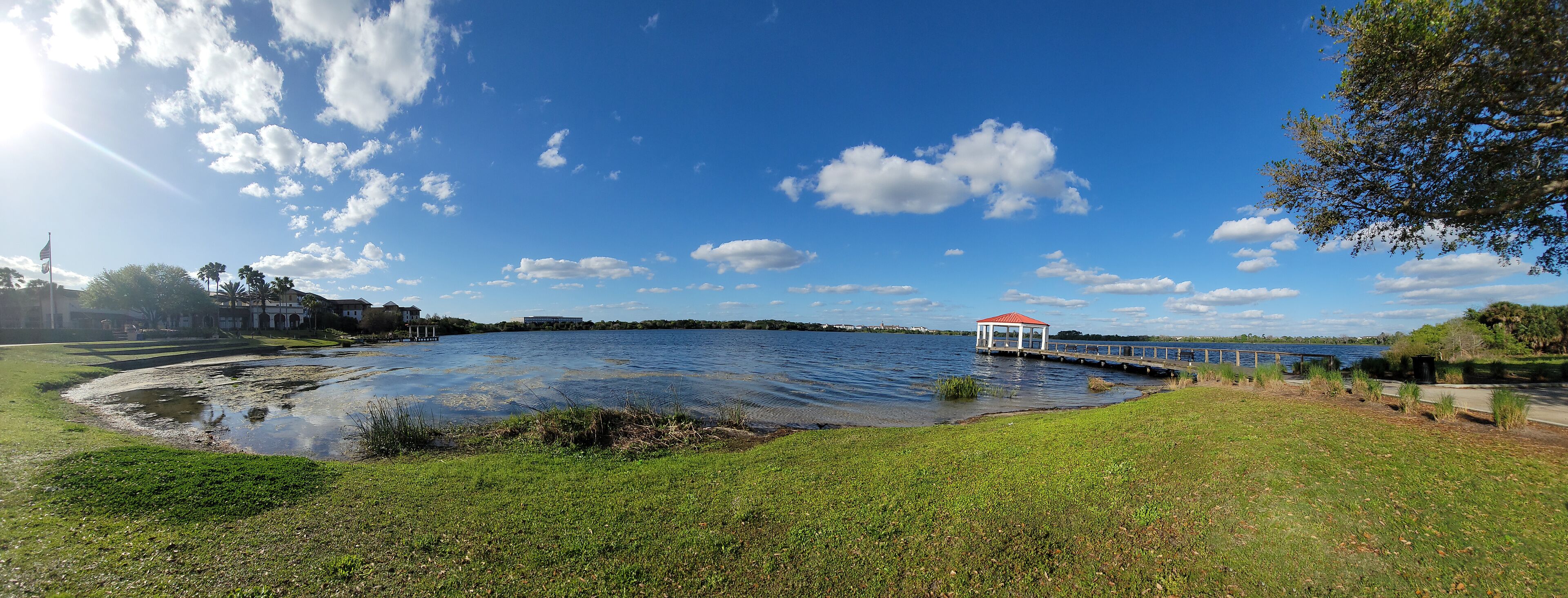 Um lago com um coreto, margens gramadas e um céu azul límpido.