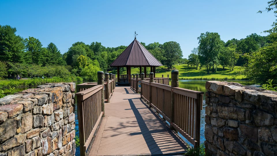 A wooden bridge with a gazebo, stone walls, and a lake surrounded by trees.