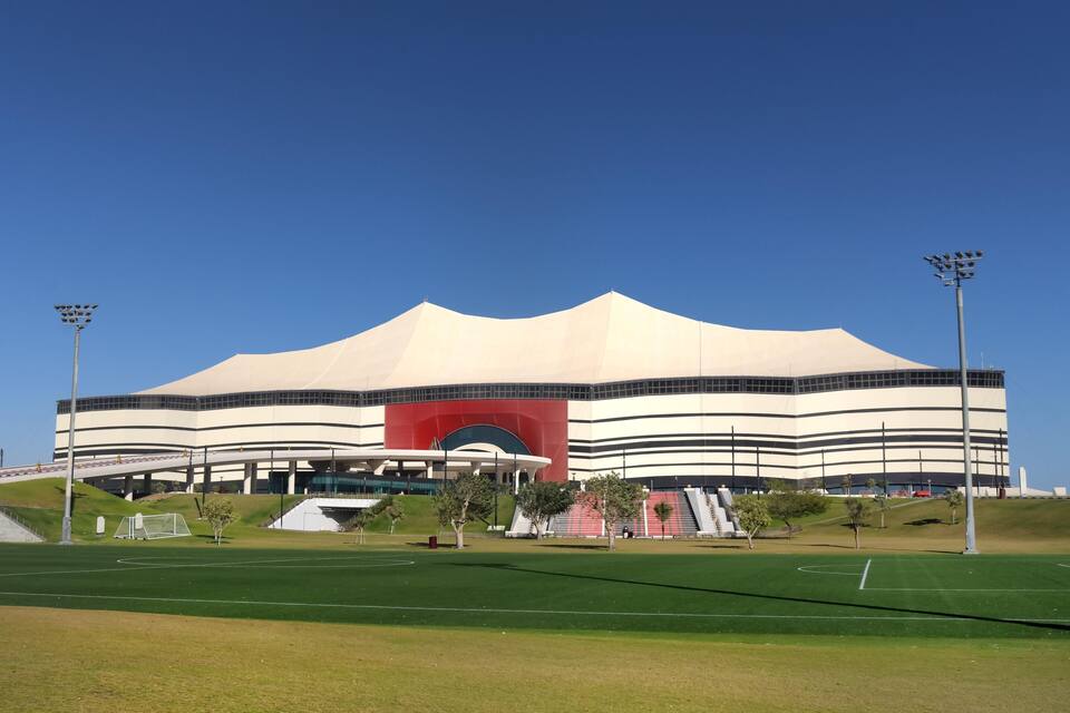 A large stadium with a distinctive red arch and white exterior.