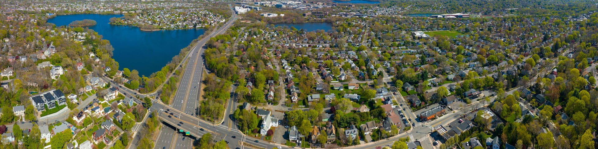 Arlington Heights suburban landscape panoramic aerial view in spring with Spy Pond and Boston modern city skyline at the background in historic town of Arlington, Massachusetts MA, USA.