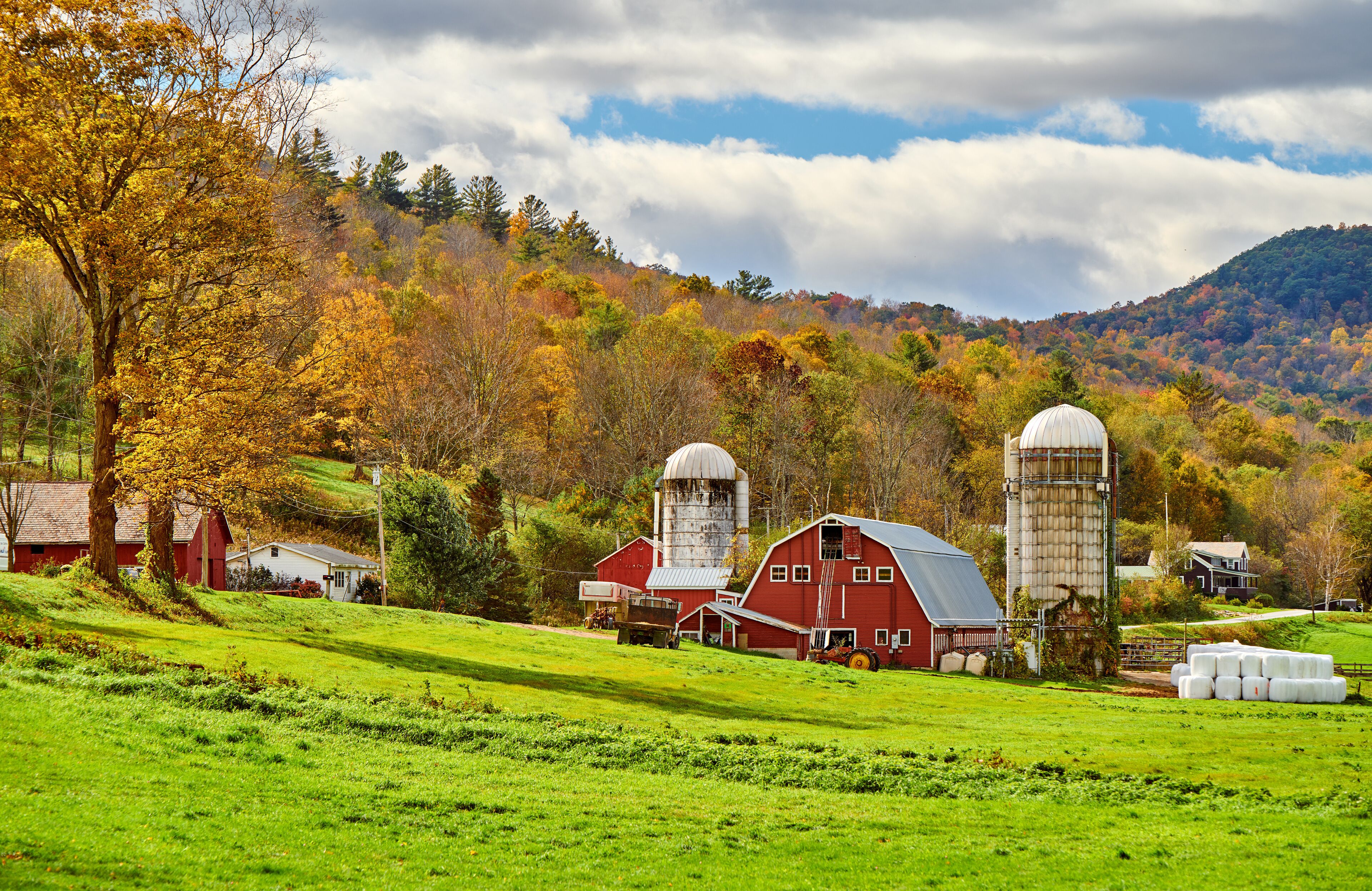 A rural landscape with barns, silos, and autumn-colored trees.