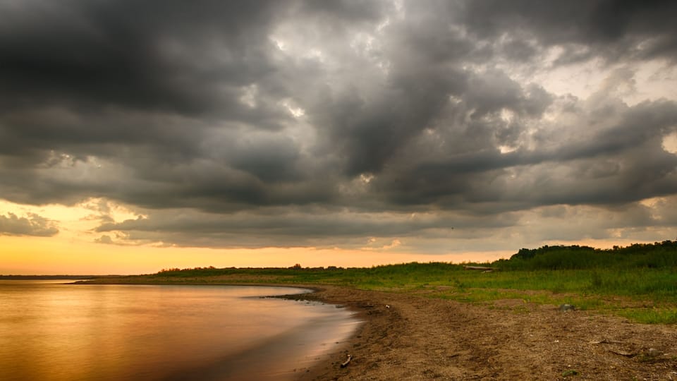 A riverbank with a grassy area and a cloudy sky.