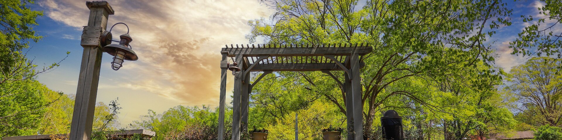 a gorgeous summer landscape with a brown wooden awning at the top of a staircase surrounded by a hillside covered with lush green trees, grass and plants with blue sky and powerful clouds at sunset