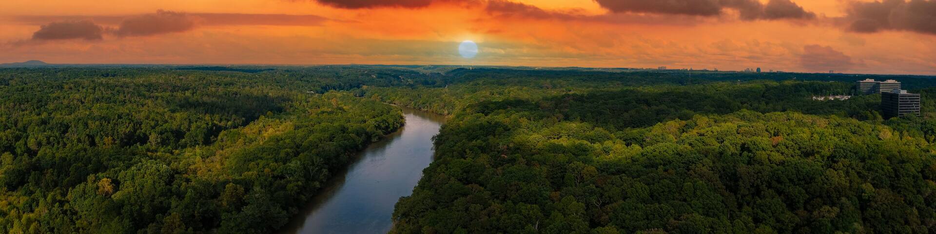 a stunning aerial panoramic shot of the Chattahoochee river surrounded by lush green and autumn colored trees with powerful clouds at Cochran Shoals Trail in Marietta USA