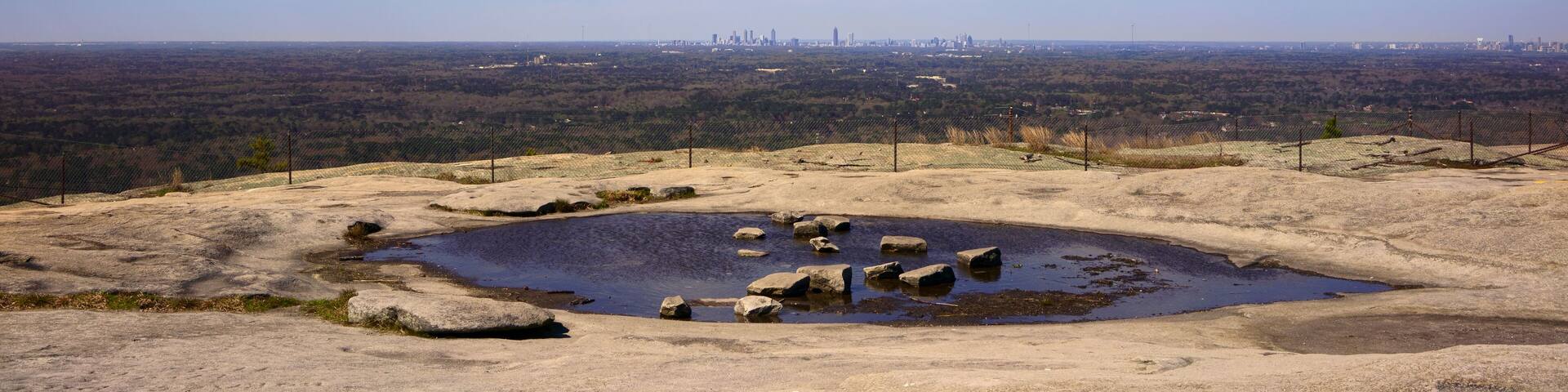 On top of Stone Mountain in Stone Mountain Park near Atlanta, Georgia, USA. Landscape of bare rock with rock pools and panorama view of the downtown Atlanta skyline.