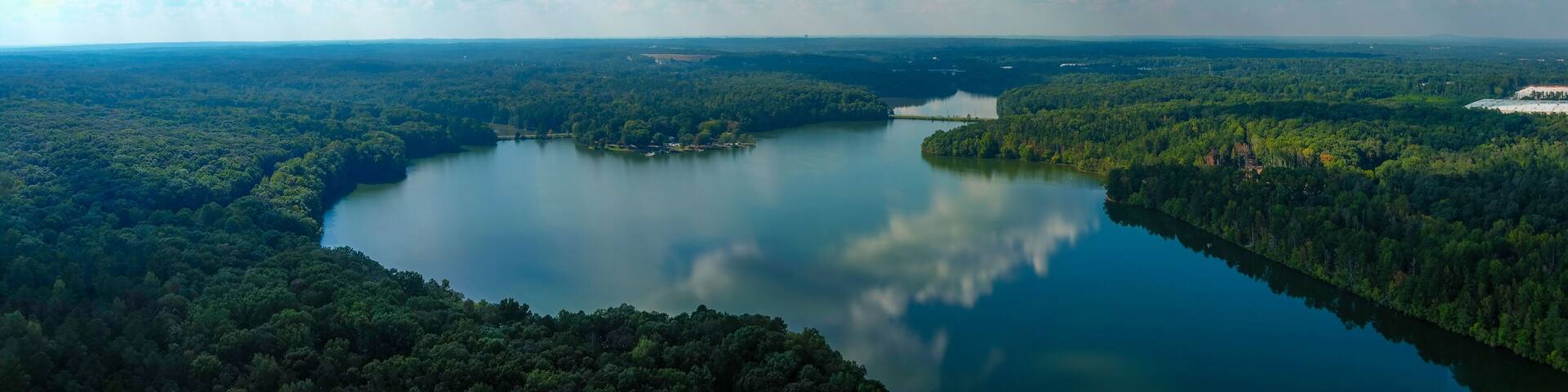 stunning aerial shot of the still blue waters of the lake with blue sky and clouds reflecting off the water and vast miles of lush green trees at Sweetwater Creek State Park in Lithia Springs Georgia