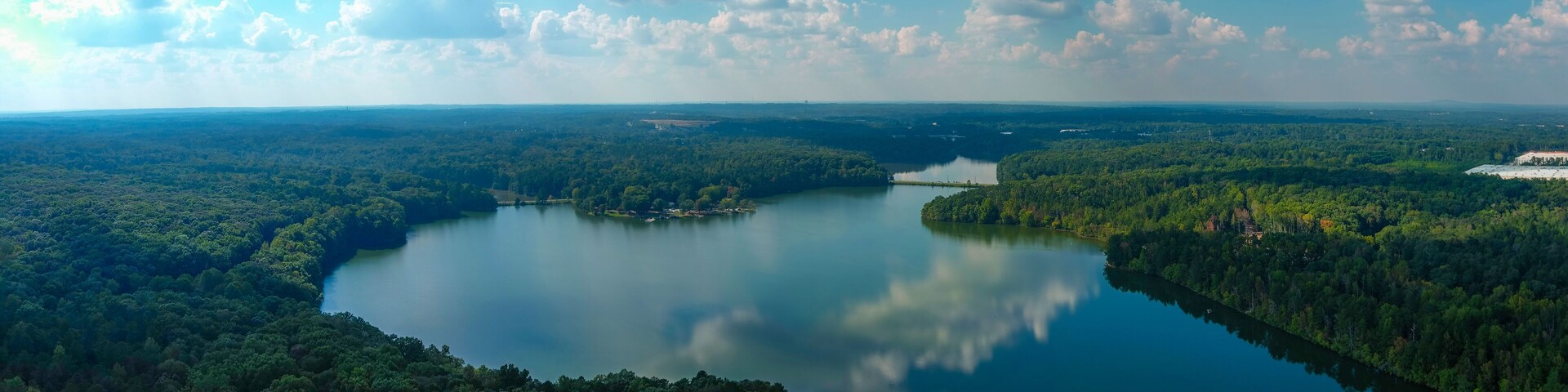 stunning aerial shot of the still blue waters of the lake with blue sky and clouds reflecting off the water and vast miles of lush green trees at Sweetwater Creek State Park in Lithia Springs Georgia