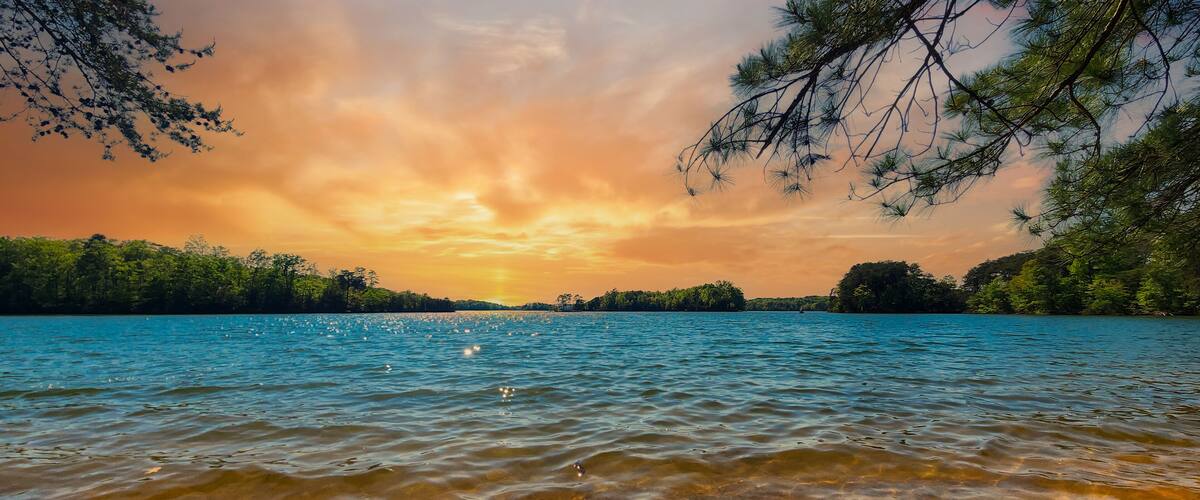 A lake with clear water, surrounded by trees and a sunset sky.