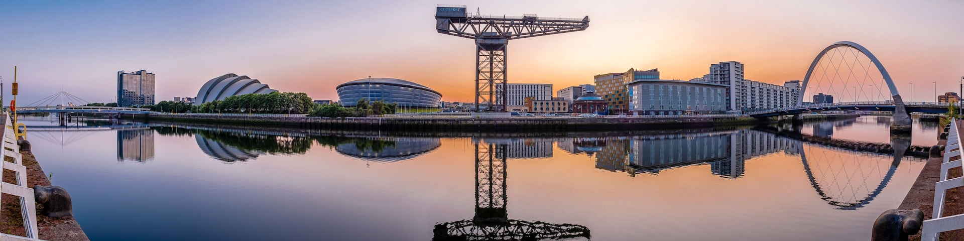 Un horizonte urbano con una noria gigante, edificios modernos y un río tranquilo que refleja las construcciones.