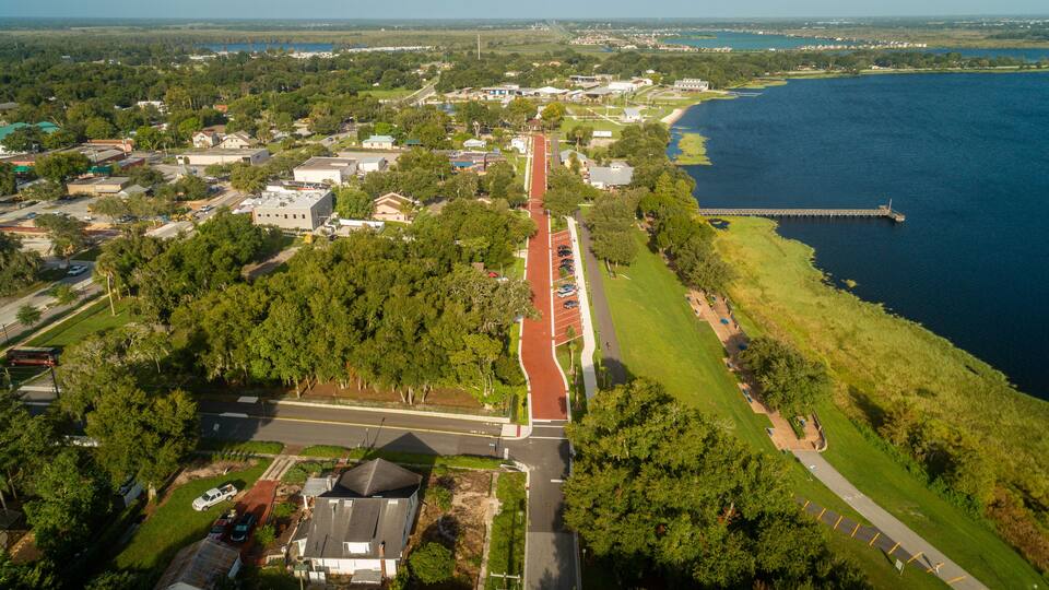 An aerial view of a coastal town with a red running track, green parks, and a marina.