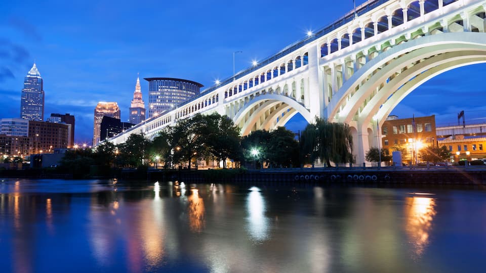 A bridge with multiple arches over a body of water, reflecting city lights and buildings.